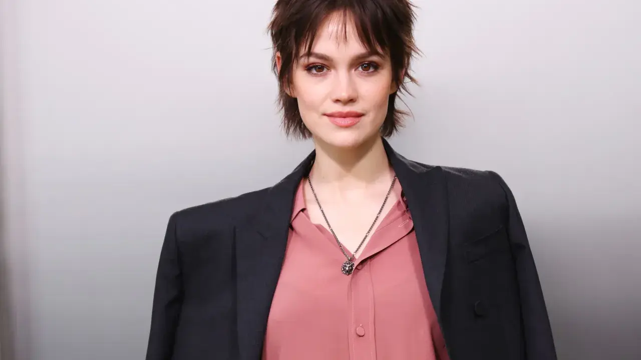 Junge Frau mit modischer Kurzhaarfrisur, inspiriert von Frisuren ab 50. Sie trägt einen rosafarbenen Blusen- und dunklen Blazer-Look.