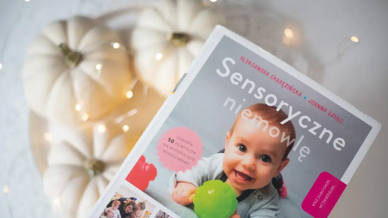 Okładka książki "Sensoryczne niemowlę" z uśmiechniętym dzieckiem, dyniami i lampkami.