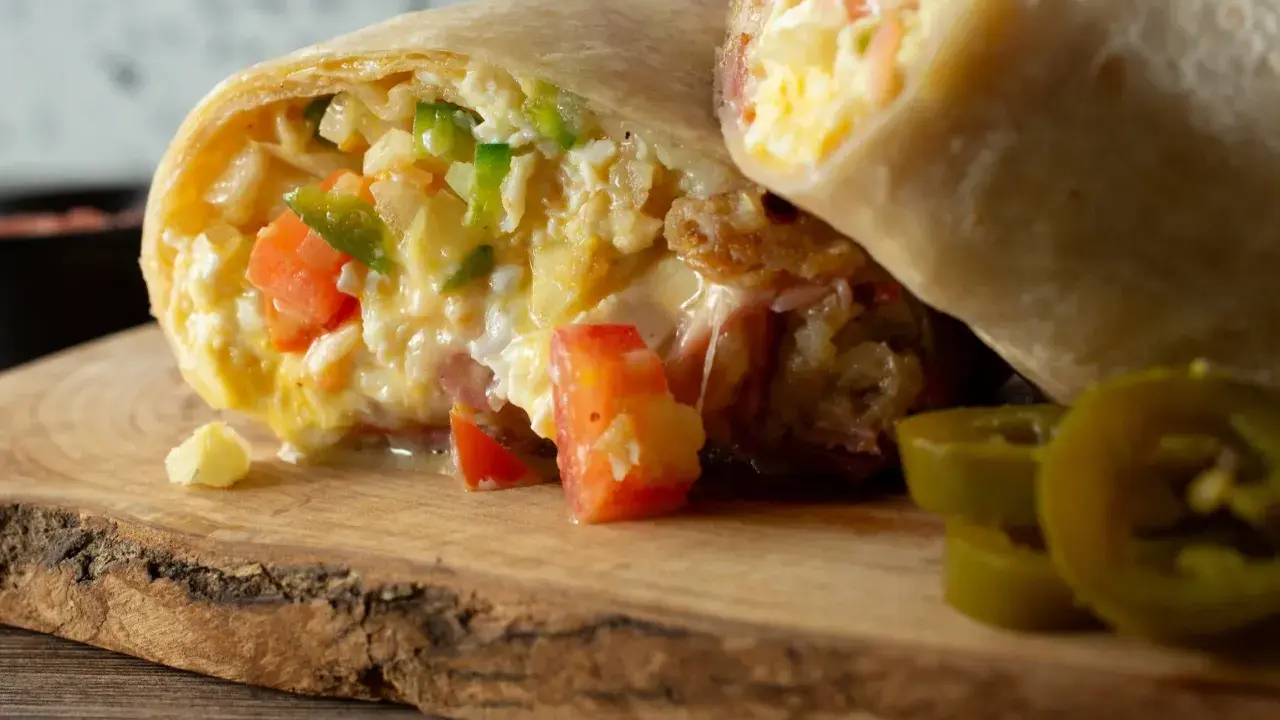 Pyszna tortilla z jajecznicą, pomidorami i papryką, podana na drewnianej desce z plasterkami jalapeno.