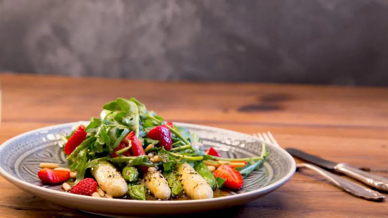 Ein frischer Spargelsalat mit Erdbeeren, Rucola und Pinienkernen, appetitlich auf einem Teller angerichtet.