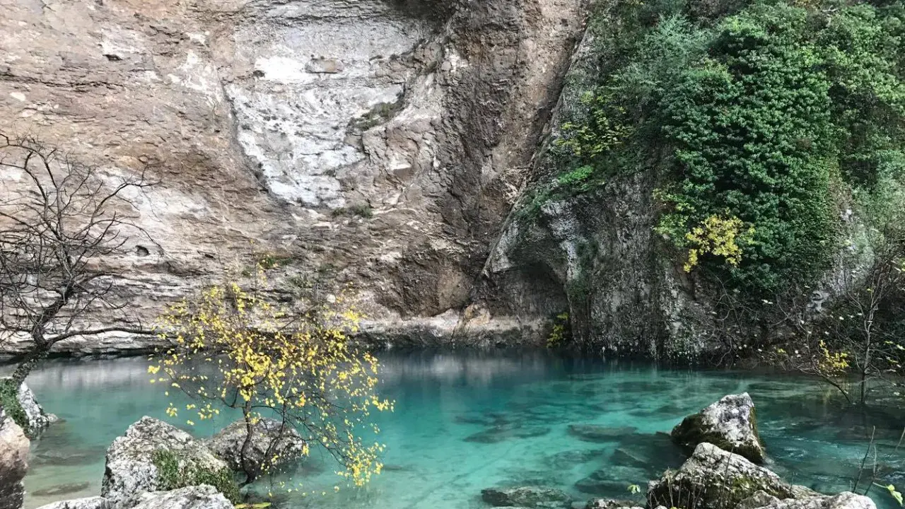 La source de la Sorgue, une eau turquoise limpide émergeant d'une falaise rocheuse, entourée de végétation et d'arbres aux feuilles d'automne.