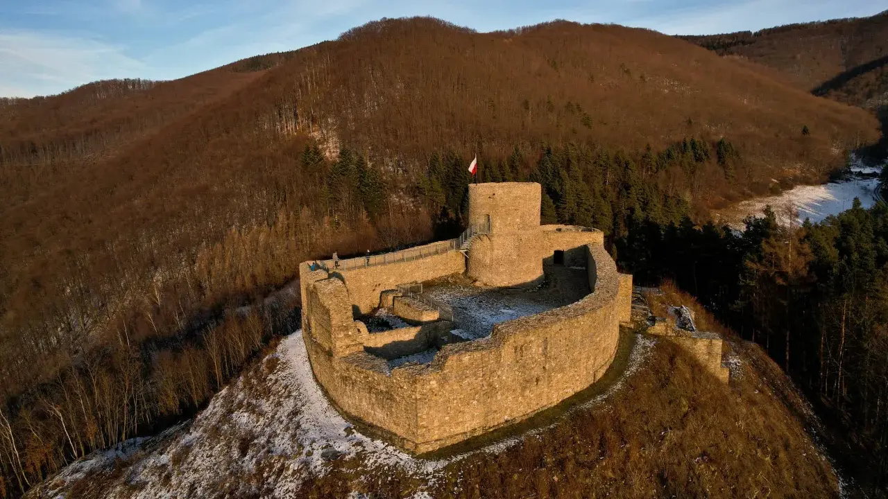 Ruiny zamku w Rytrze, z polską flagą na wieży. Warto sprawdzić zamek w Rytrze cennik przed wizytą.