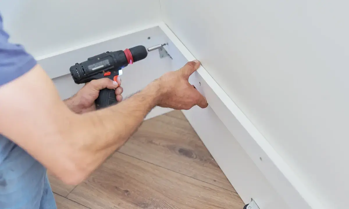 Pose d'une placo sur ossature bois. Un artisan utilise une visseuse pour fixer une plaque de plâtre sur une structure en bois.