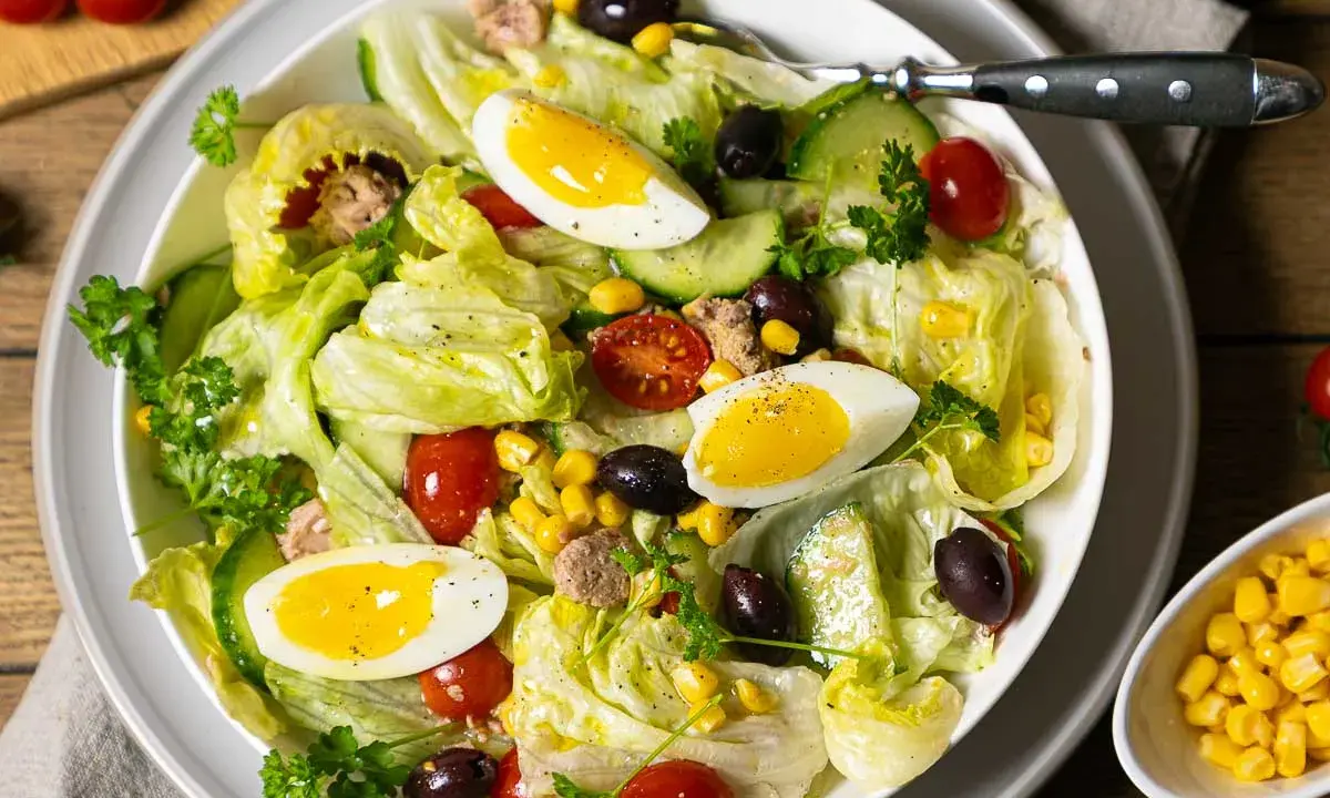 Frischer Salat mit knackigem Eisbergsalat, Tomaten, Gurken, Oliven, Mais und Eiern. Ein herzhafter Thunfischsalat, der Lust auf mehr macht.