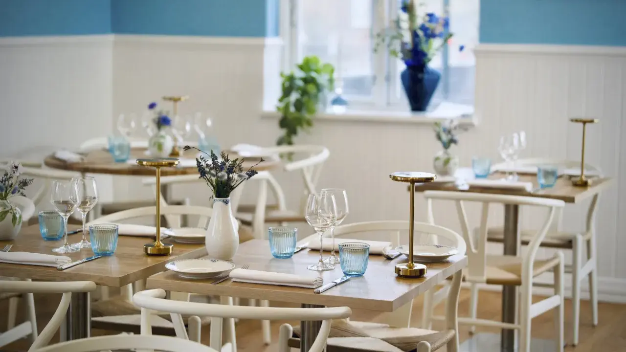 Vackert dukade bord med blåa glas och blommor i vaser, redo för gäster på en av restaurangerna i Skagen.