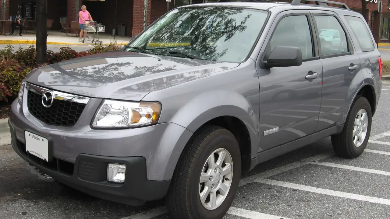 Szary Mazda Tribute zaparkowany na parkingu przed sklepem.