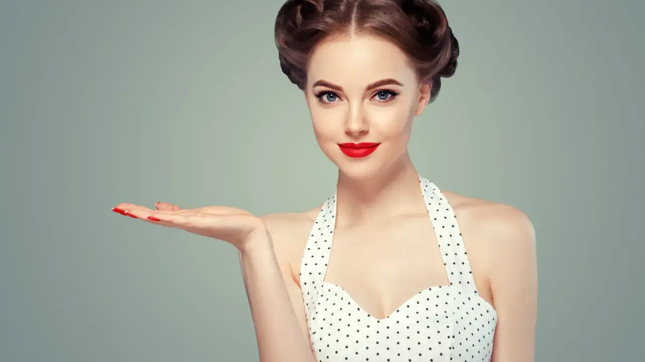 Kobieta w stylu pin up, z burzą loków i czerwoną szminką, prezentuje dłoń. To lata 50. w pełnej krasie.