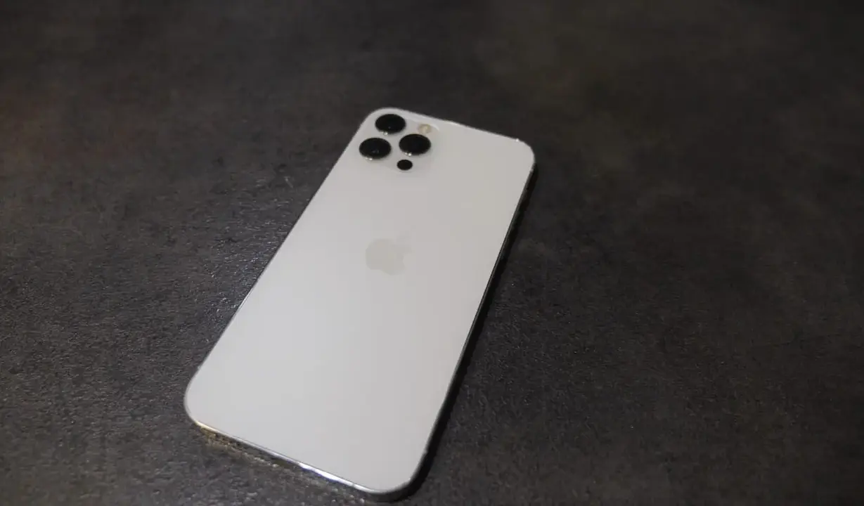 Elegancki, biały iPhone 12 Pro Max z charakterystycznym modułem aparatów na ciemnym tle.