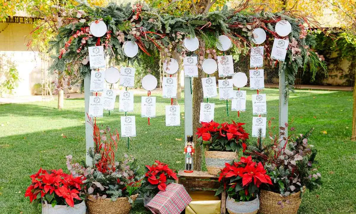 Decoración ceremonia civil con un arco de ramas y hojas, colgando tarjetas de invitados. Flores rojas y cestas adornan la base.