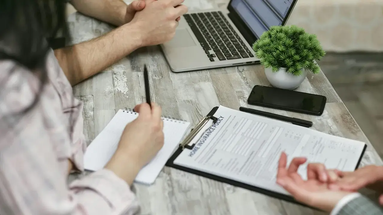 Réunion pour une contre-expertise assurance : un contrat est sur la table, un ordinateur portable ouvert, et des mains discutent des détails.