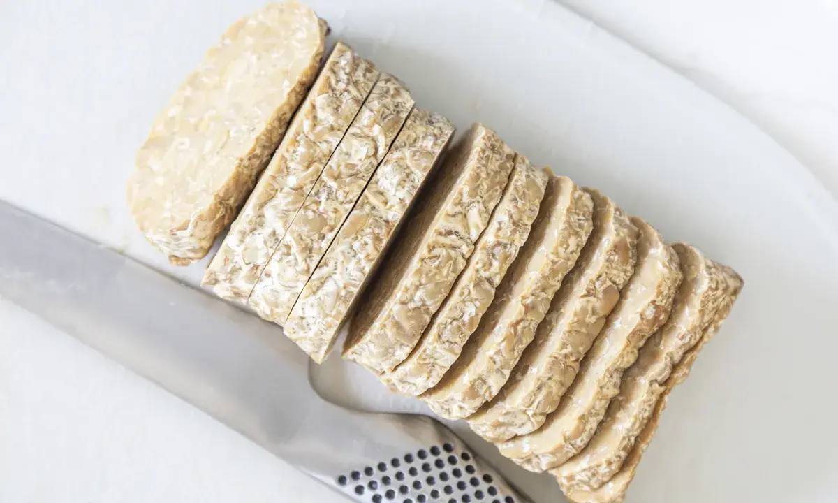 Pokrojony w plastry tempeh, czyli fermentowana soja, leży obok noża. To świetny składnik do wegańskich potraw.