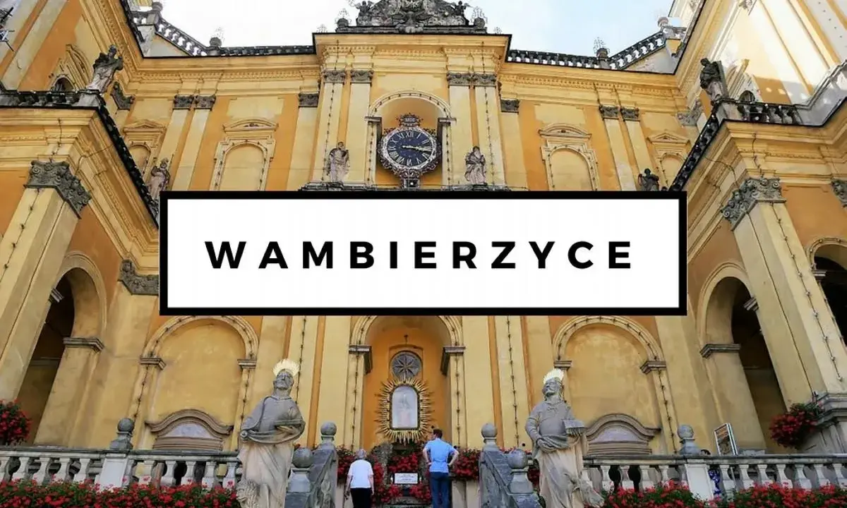 Bazylika w Wambierzycach, znana z licznych atrakcji, zachwyca architekturą. Widać schody prowadzące do sanktuarium, ozdobione czerwonymi kwiatami.