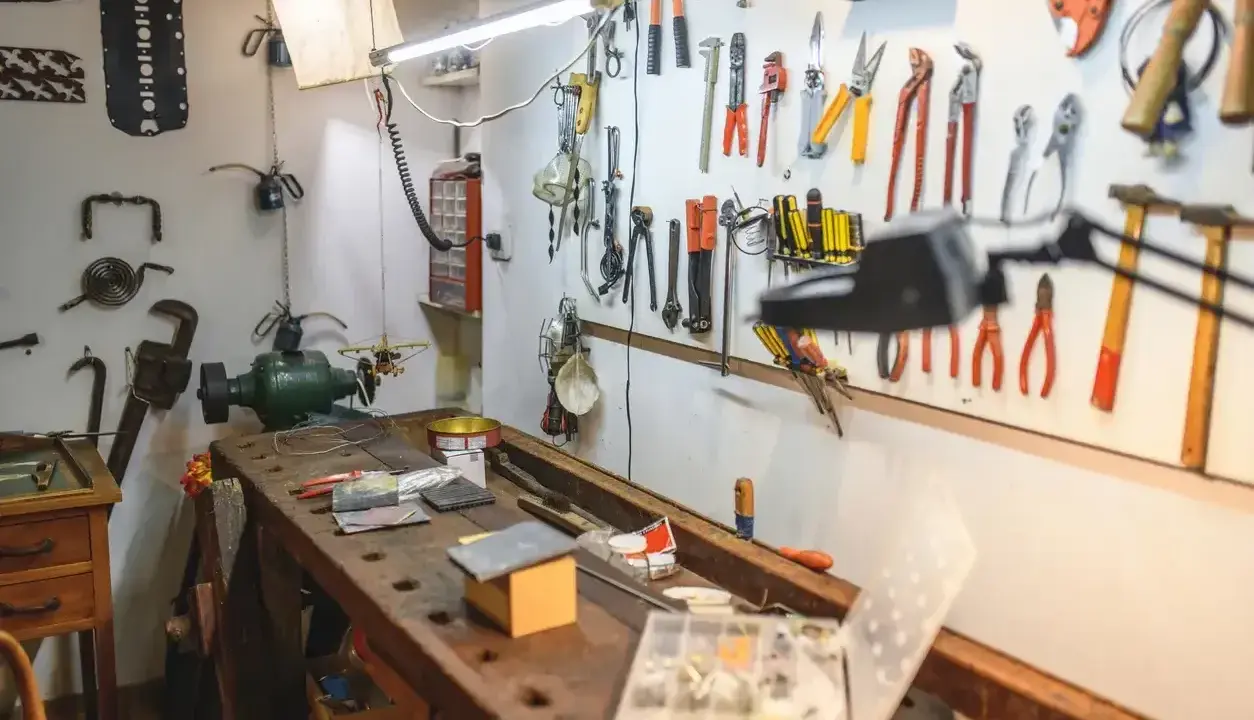 Warsztat domowy pełen narzędzi i pomysłów na majsterkowanie. Widać tu imadło, szlifierkę, mnóstwo kluczy, śrubokrętów i innych przyrządów.