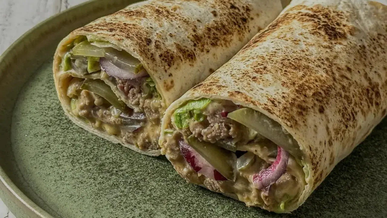 Zwei saftige Big Mac Wraps mit Hackfleisch, Salat, Gurken und Zwiebeln auf einem grünen Teller.