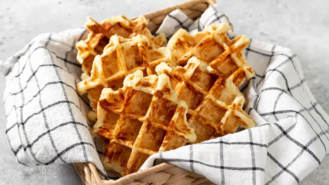 Un panier rempli de gaufres dorées, parfaites pour une recette gaufre rapide. Elles sont présentées sur une serviette à carreaux noirs et blancs.