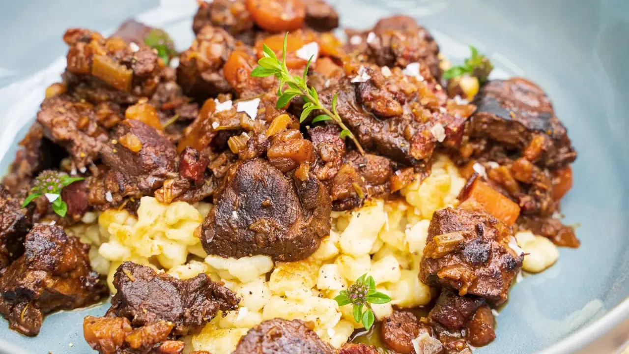 Herzhaftes Wildschwein Gulasch Rezept mit Spätzle, garniert mit frischen Kräutern und grobem Salz. Ein Genuss für Feinschmecker!