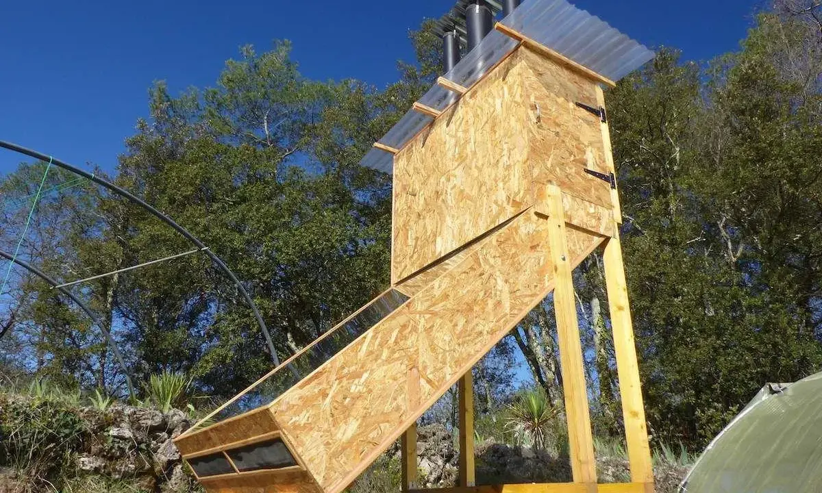 Un sechoir solaire artisanal en bois, avec un panneau incliné vitré, sous un ciel bleu.