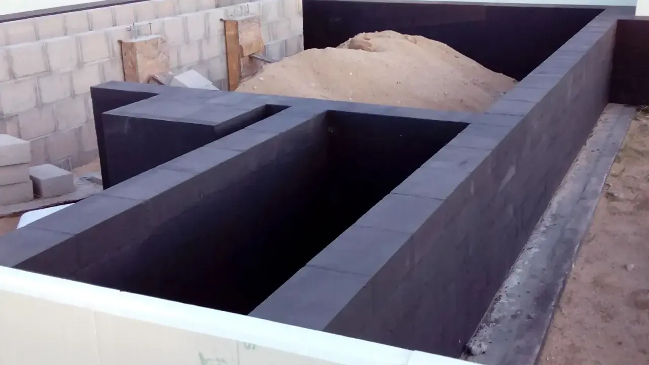 Fundament budowy z ciemnych bloczków, z nasypem piasku wewnątrz.