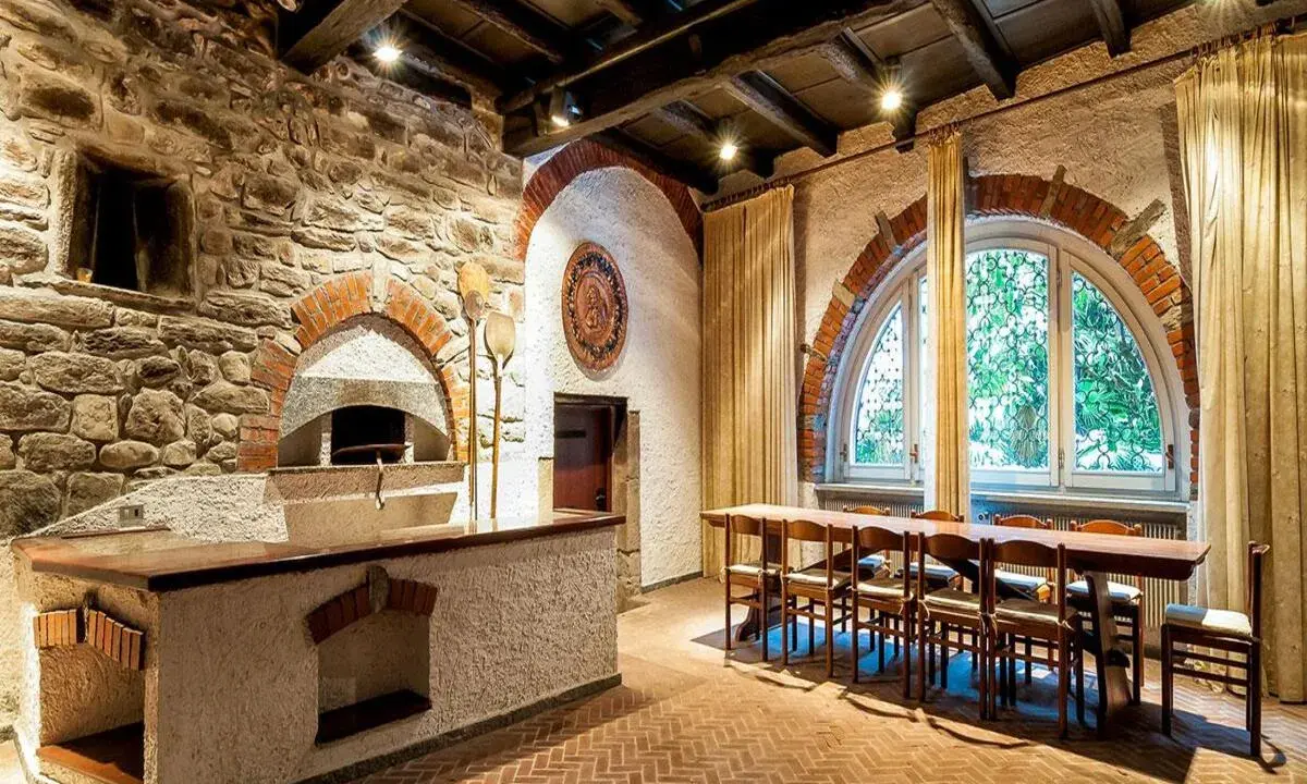 Tavernetta moderna piccola con forno a legna in pietra, bancone in muratura e un lungo tavolo in legno con sedie.