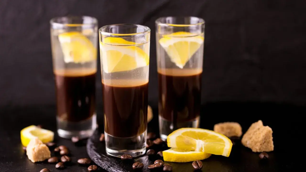 Drei Gläser mit Espresso und Zitrone, ein italienischer Genuss. Kaffeebohnen und Zuckerwürfel liegen daneben.