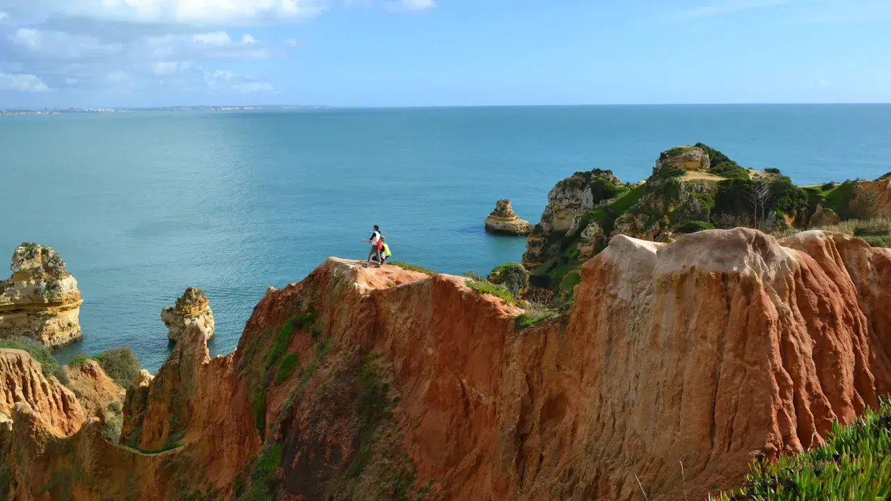 Zwei Wanderer genießen die milden Temperaturen Portugals im November an einer Klippe mit Blick auf das Meer.