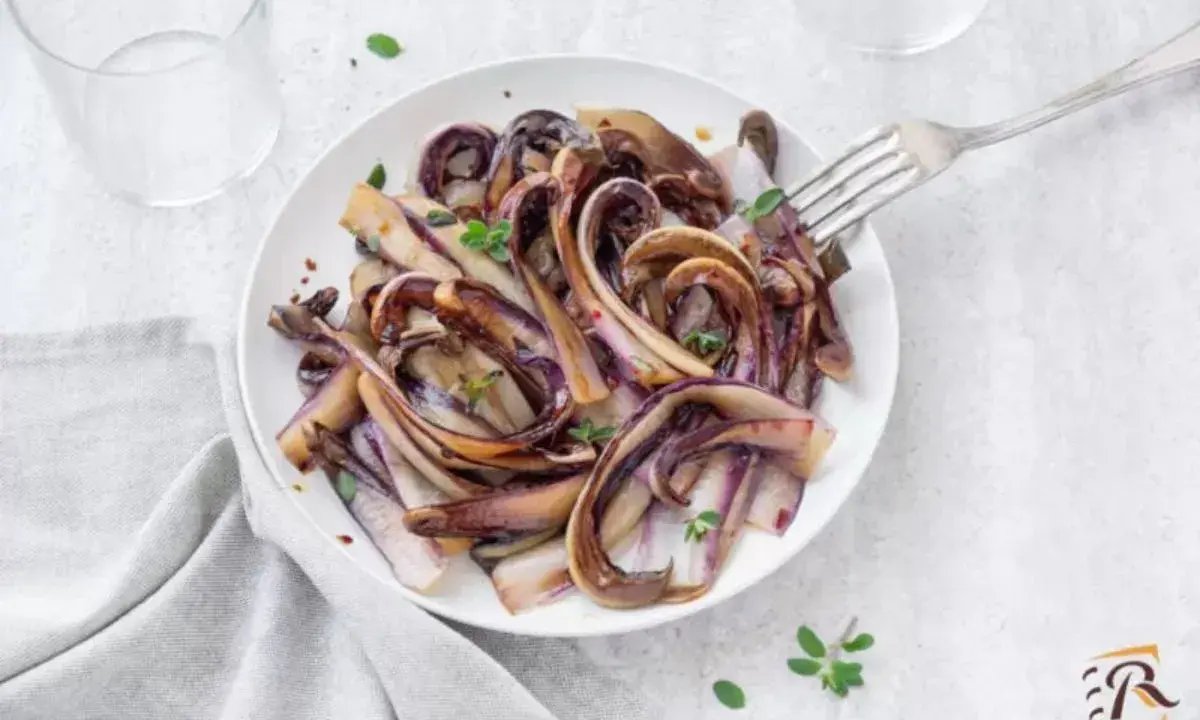 Radicchio in padella, caramellato e profumato, servito su un piatto bianco con un tocco di erbe aromatiche.
