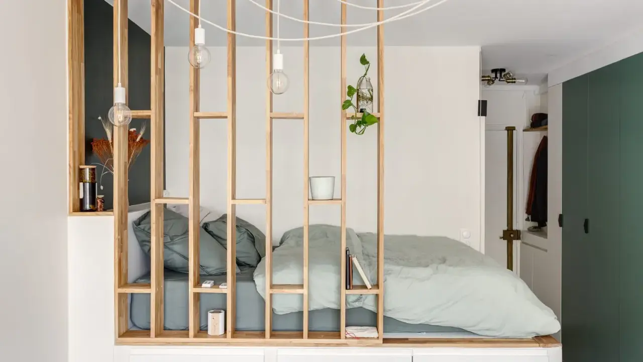 Aménagement astucieux d'un studio T2 avec un lit douillet séparé par une étagère en bois.