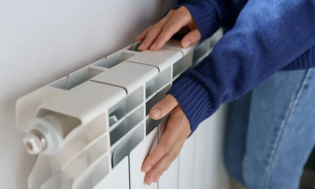 Manos frías tocan un radiador blanco que no calienta.