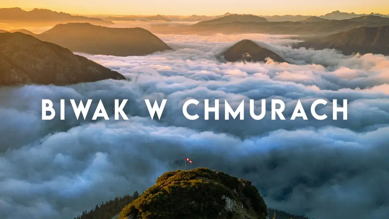 Widok z gór podczas trekkingu w Austrii. Chmury otulają szczyty, a na jednym z nich powiewa flaga.