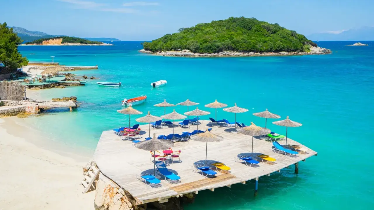 Rajskie widoki na **Albania najpiękniejsze plaże**. Turkusowa woda, piaszczysta plaża i drewniany pomost z leżakami.
