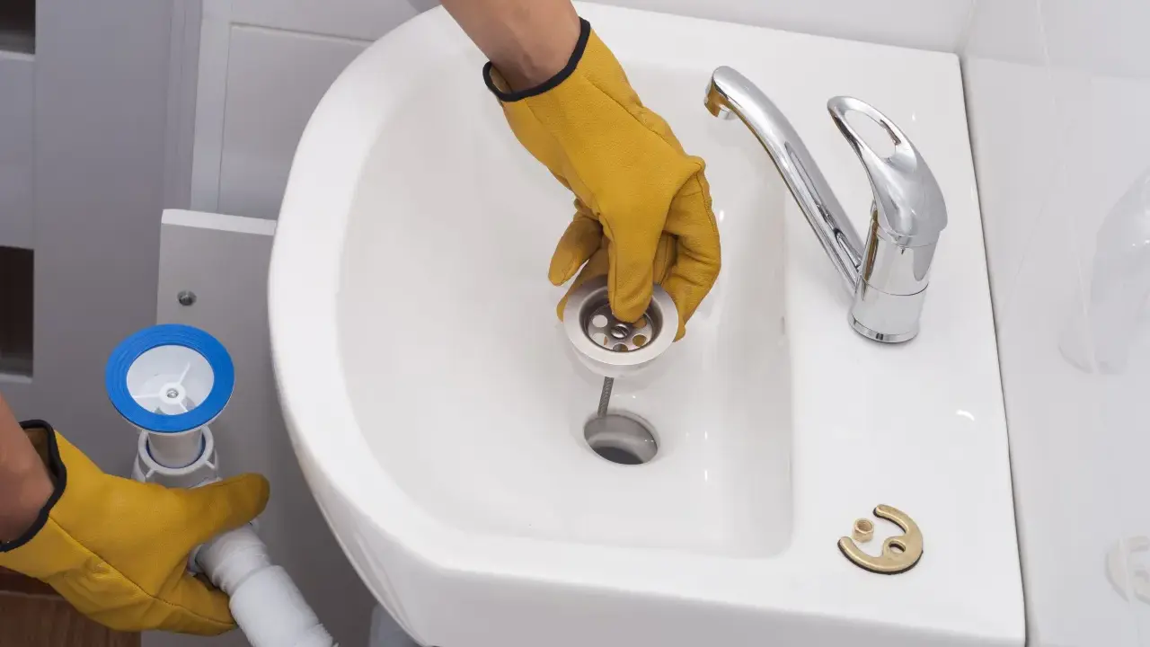 Manos enguantadas instalan el desagüe para cambiar el sifón del lavabo.