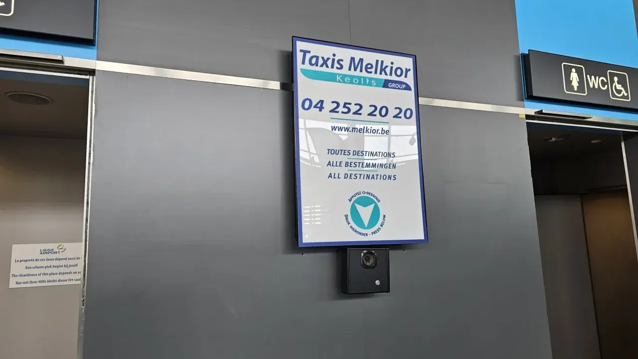 Taxi Melkior-skylt vid lgg flygplats. En övervakningskamera är monterad under skylten.