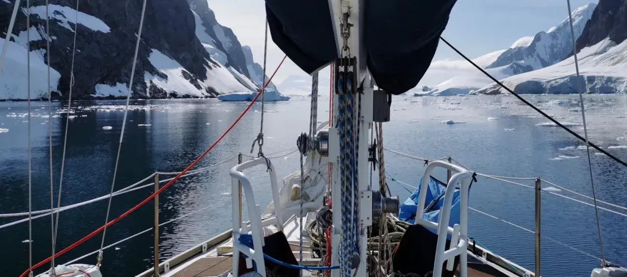 Voile sur un voilier dans un fjord glacé, avec des montagnes enneigées et des icebergs. Le **pen duick 600** navigue paisiblement.