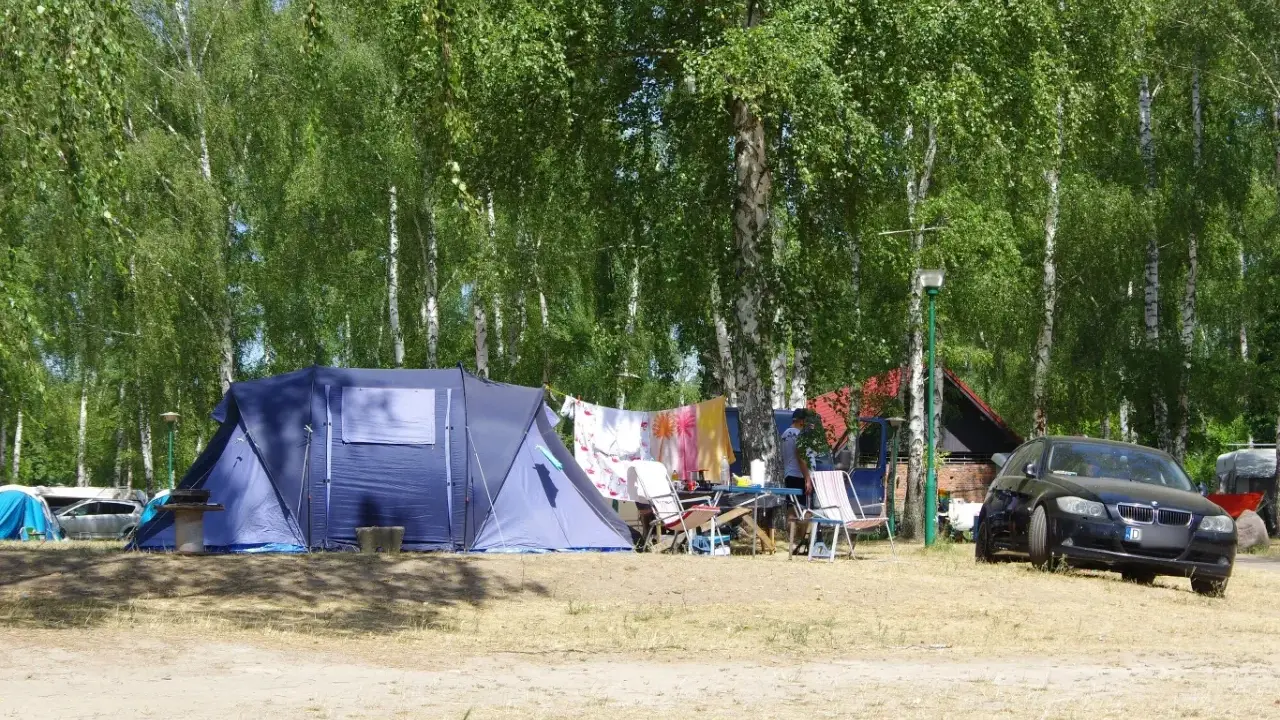 Idealne miejsce, gdzie pod namiot nad jezioro. W tle las, a przed namiotem rozłożone krzesła i suszące się pranie.