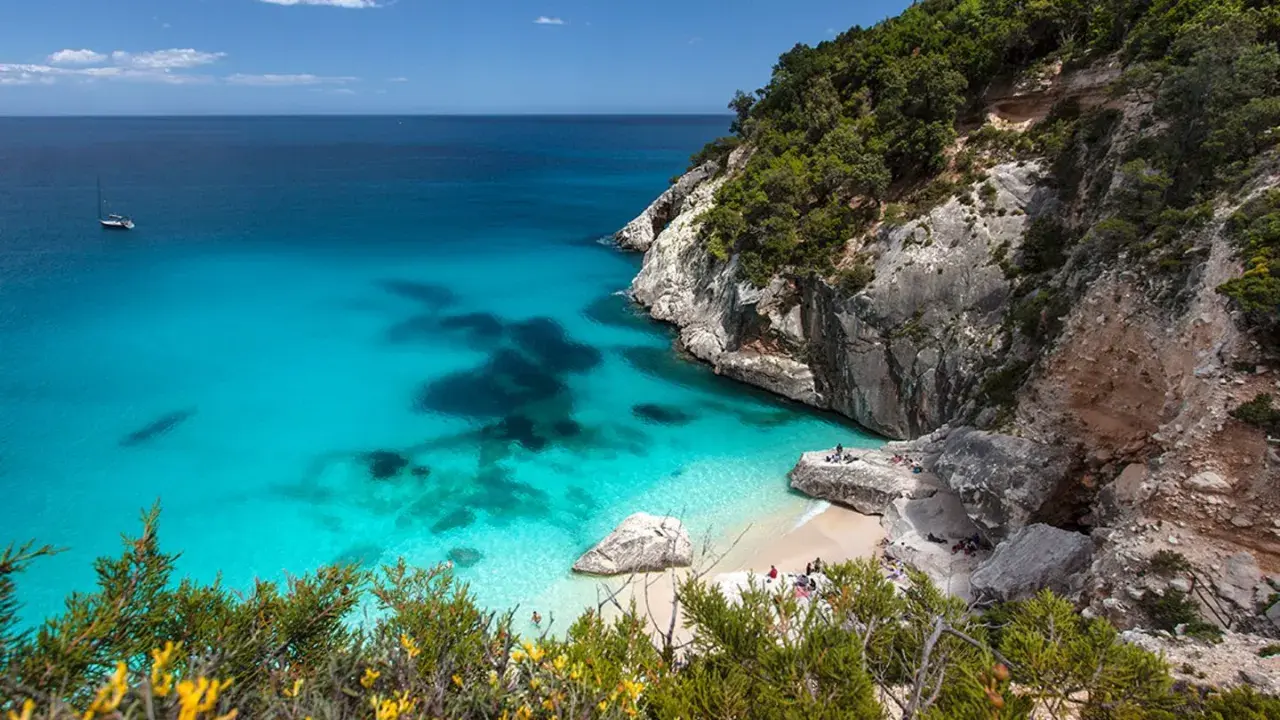 Traumhafter Strand Sardinien mit türkisfarbenem Wasser, Felsen und grüner Vegetation. Eine kleine Bucht lädt zum Entspannen ein.