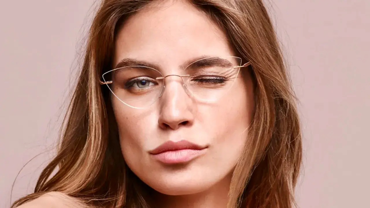 Eleganckie okulary korekcyjne bez oprawek podkreślają spojrzenie kobiety, która mruga do obiektywu.