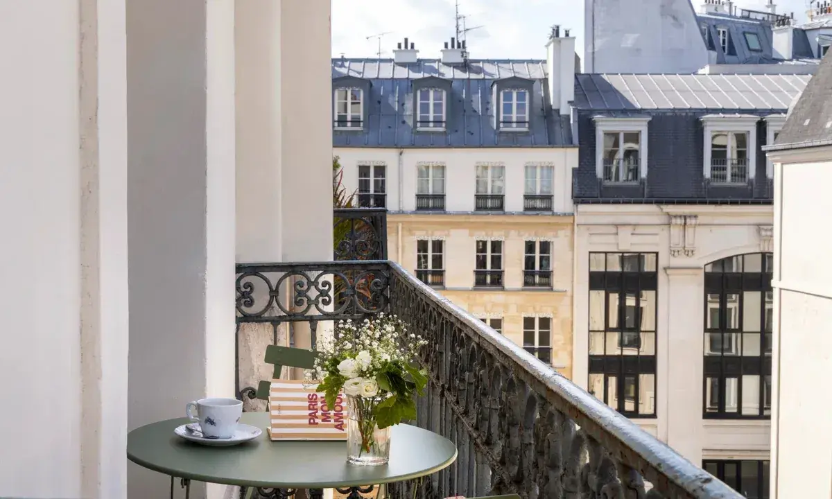 Petit-déjeuner sur le balcon avec vue sur les toits de Paris. Une tasse de café, un livre "Paris mon amour" et des fleurs, un moment de détente au saint-grégoire.
