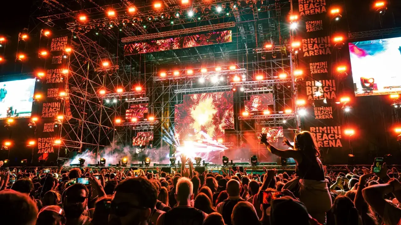 Un concerto elettrizzante alla Rimini Beach Arena. Migliaia di fan in delirio sotto un palco imponente illuminato da luci stroboscopiche e schermi giganti.