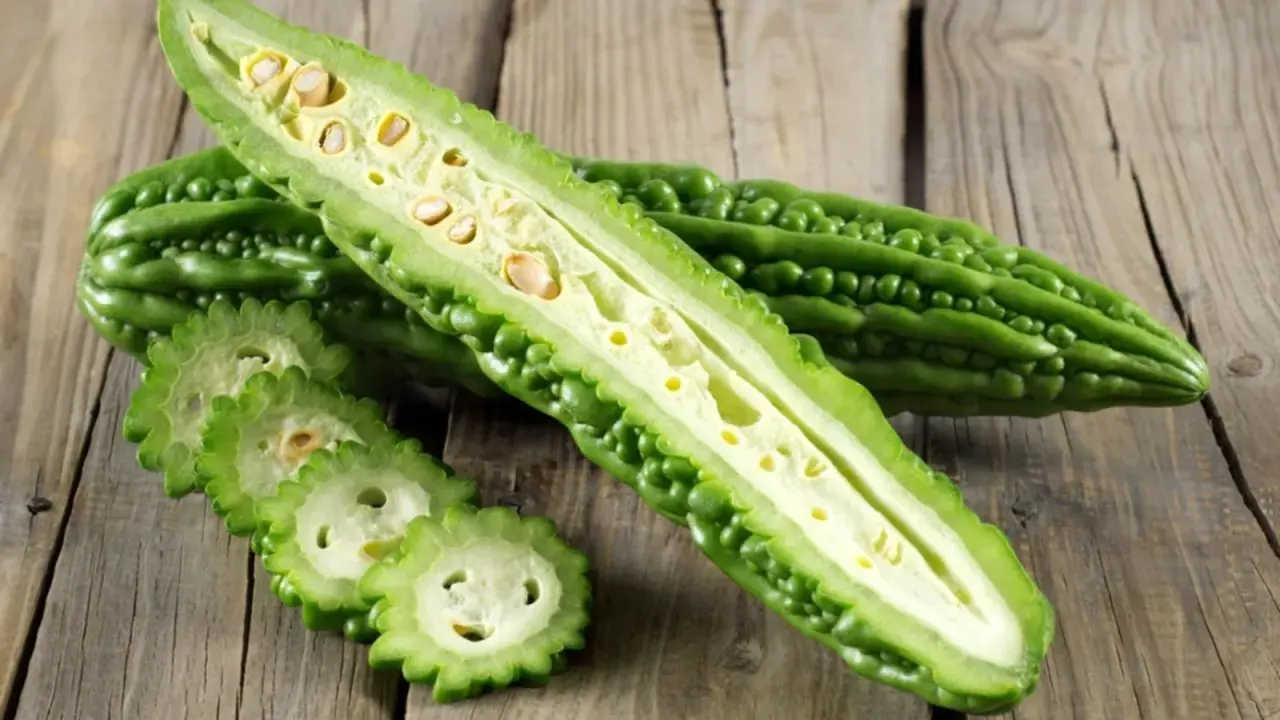 A halved bitter melon plant reveals its seedy interior, with sliced rounds fanned out on a rustic wooden surface.