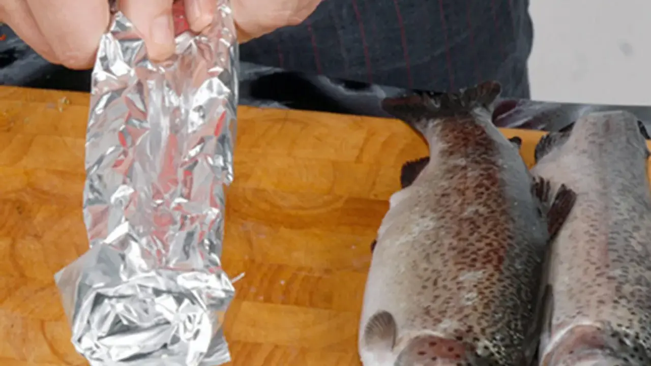 Vorbereitung für das Grillen: Ein Fisch wird in Alufolie gewickelt, bereit für den Weber Grill.