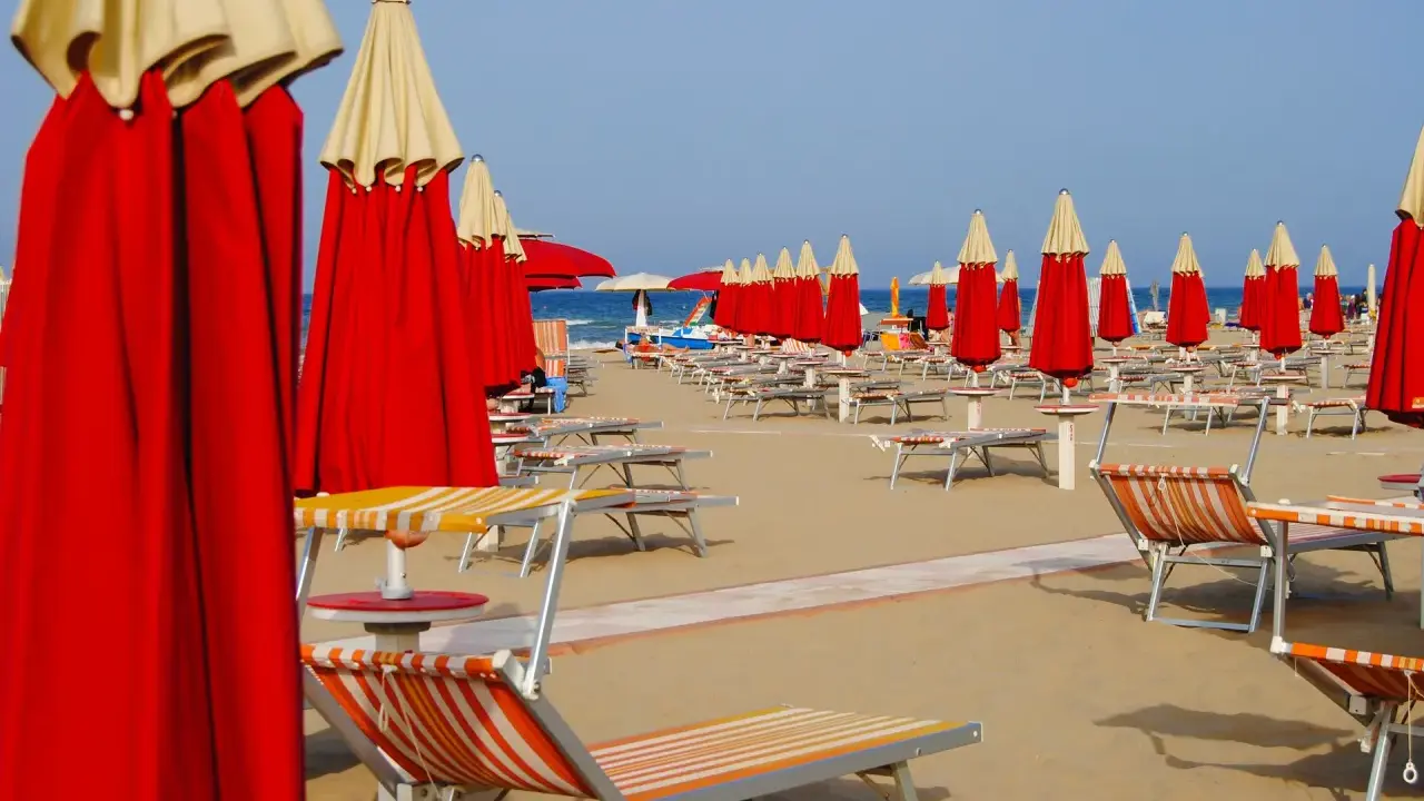 Filetto di ombrelloni rossi e lettini pronti per accogliere i bagnanti sulla costa di Rimini.