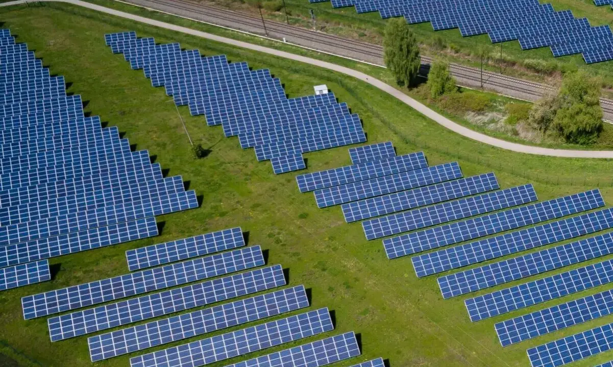 Große Solaranlage auf einer grünen Wiese mit Gleisen im Hintergrund.