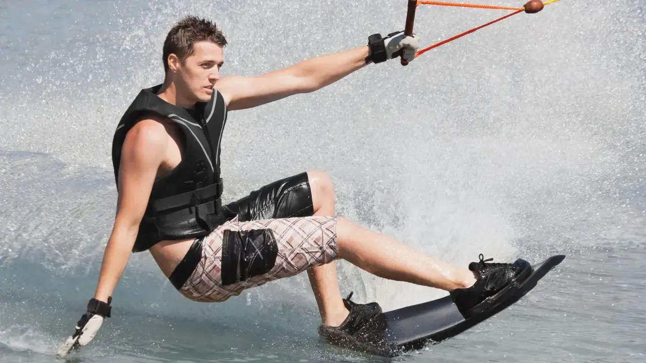 Młody mężczyzna na desce, ciągnięty przez linę, pokazuje, **wakeboarding co to** jest – sport wodny pełen adrenaliny i zabawy.
