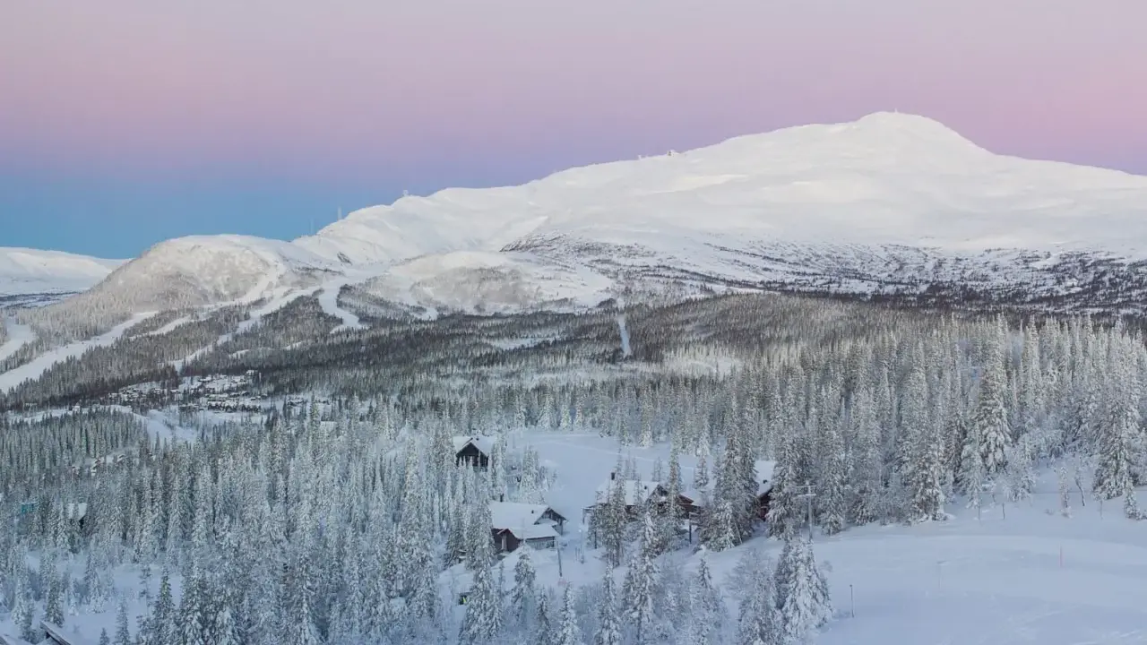 Snötäckta berg och skog med små stugor, en idyllisk vy över mindre skidorter Sverige i skymningen.