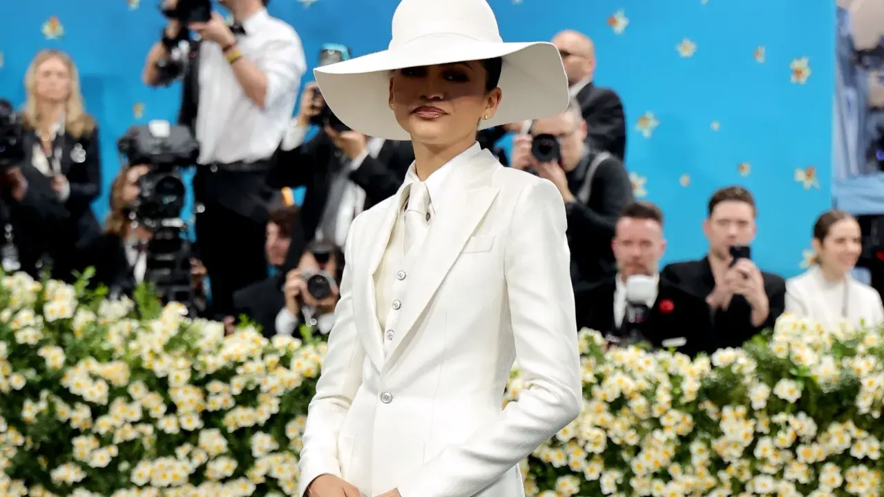 Zendaya, deslumbrante con traje blanco y sombrero, posa ante cámaras y flores.