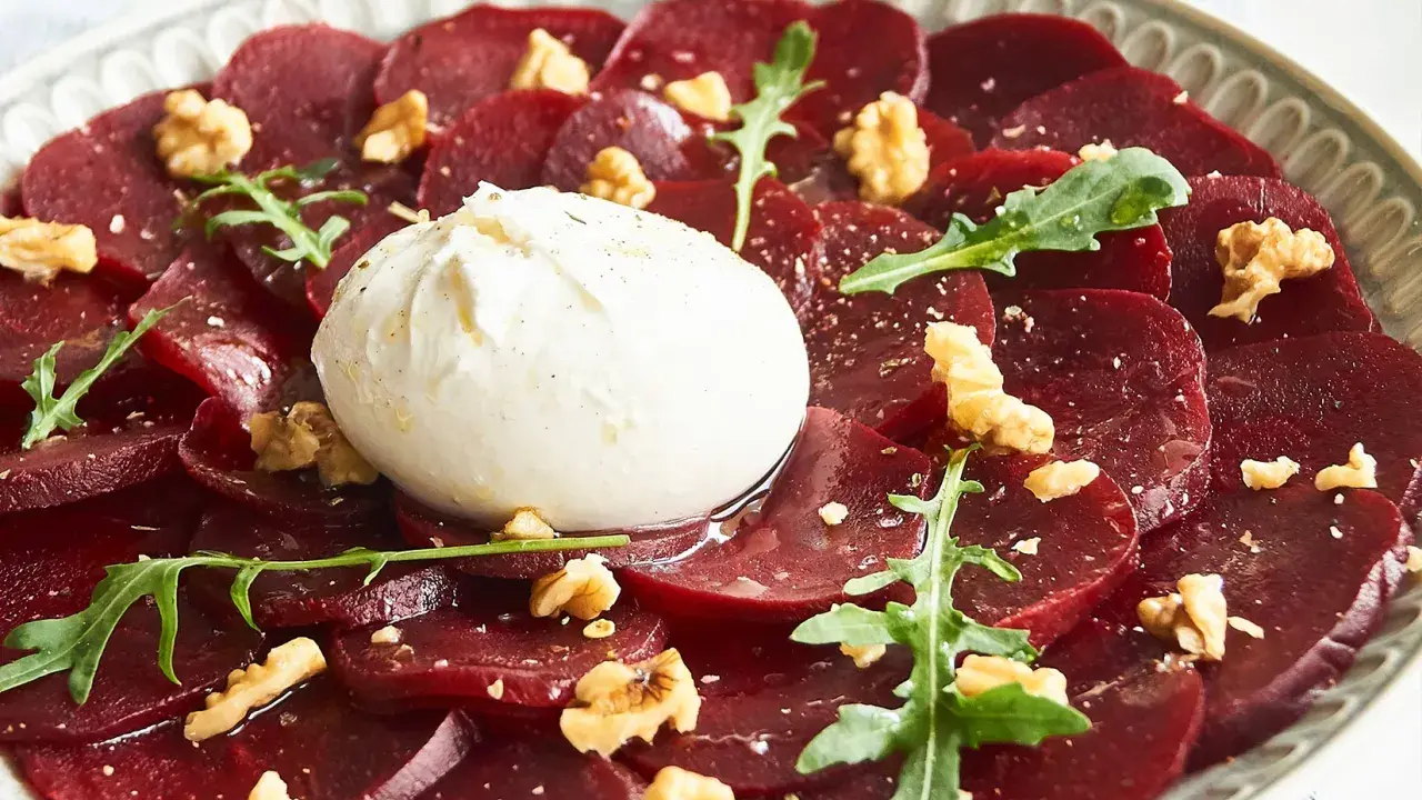 Rote Bete Carpaccio mit Burrata, Walnüssen und Rucola auf einem Teller.