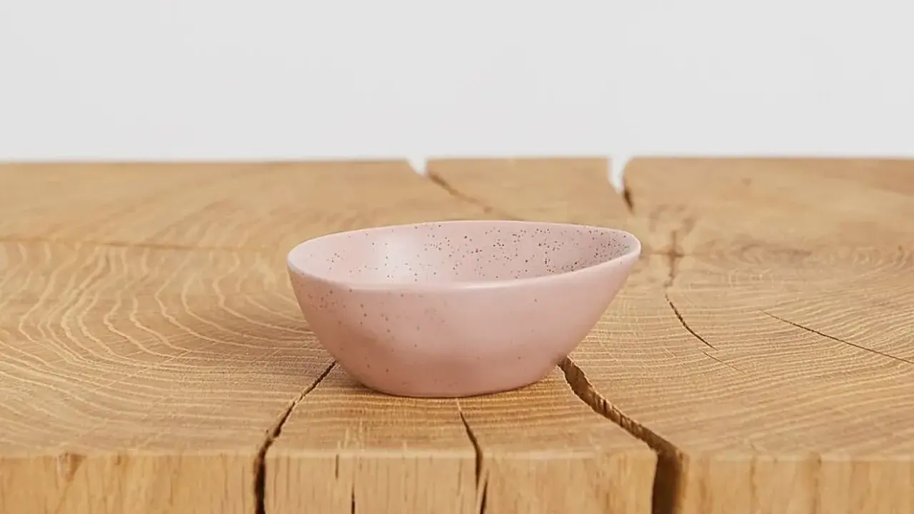 En ljusrosa skål med prickar, perfekt att skapa med lufttorkande lera. Ligger på ett träbord.