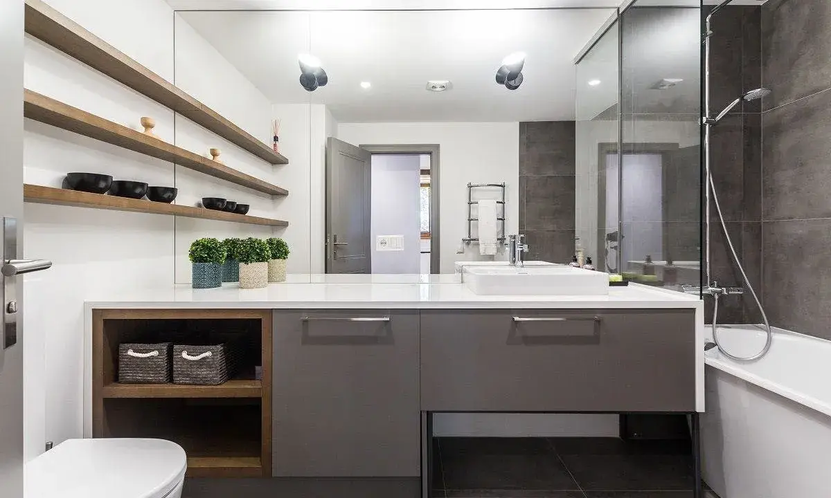 Moderno baño con ducha, bañera y lavabo sobre mueble gris. Estanterías de madera con cuencos negros. Un ejemplo de presupuesto de reforma de baño.