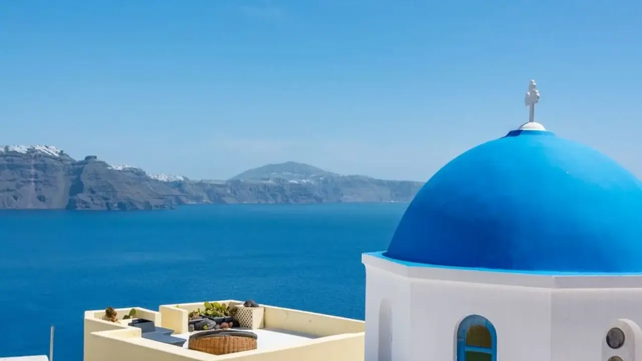 Blaue Kuppel einer Kirche in Oia, Santorini, mit Blick auf das tiefblaue Meer und die zerklüftete Küste.