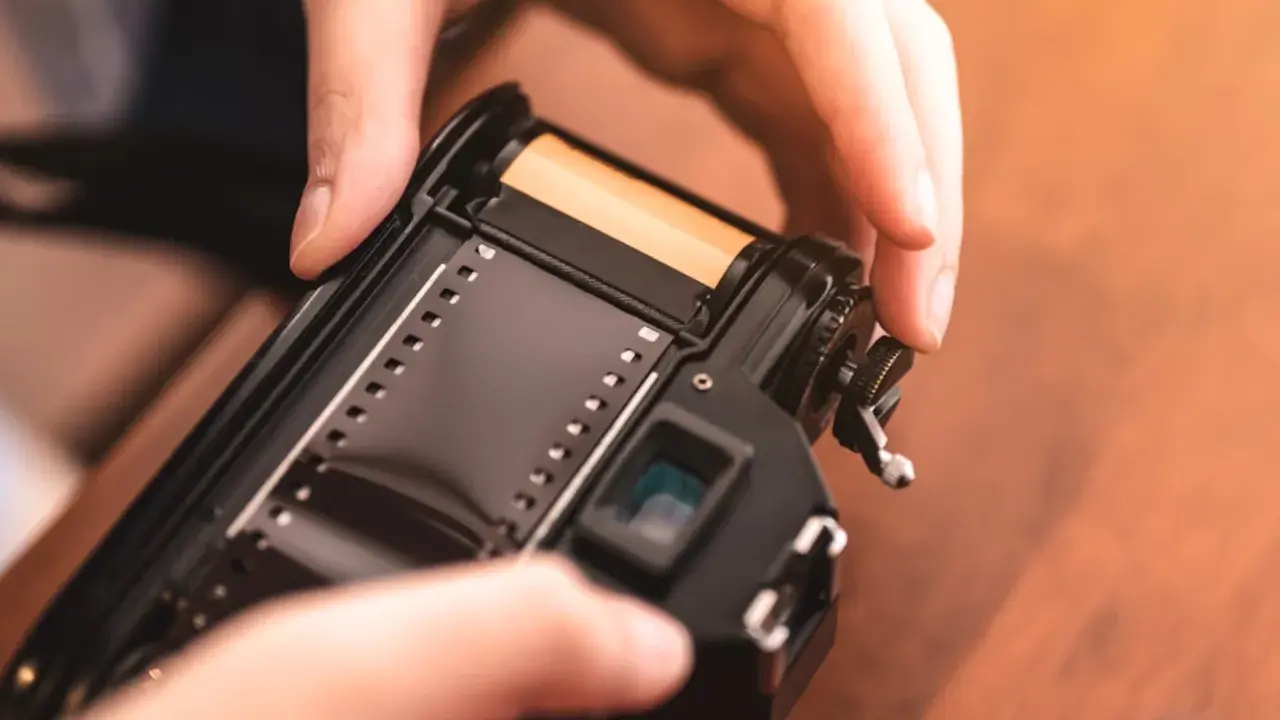 Manos insertando rollo de película en cámara analógica, un paso clave para aprender como revelar fotos en casa.